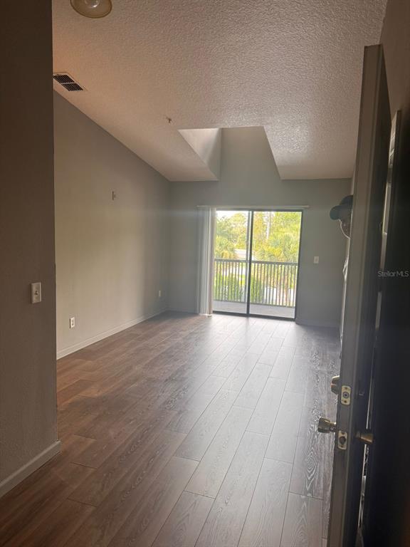 An empty living room with vaulted ceilings, wood-look flooring, and a sliding glass balcony door — 1132 S PINE RIDGE CIRCLE UNIT 32, SANFORD, FL