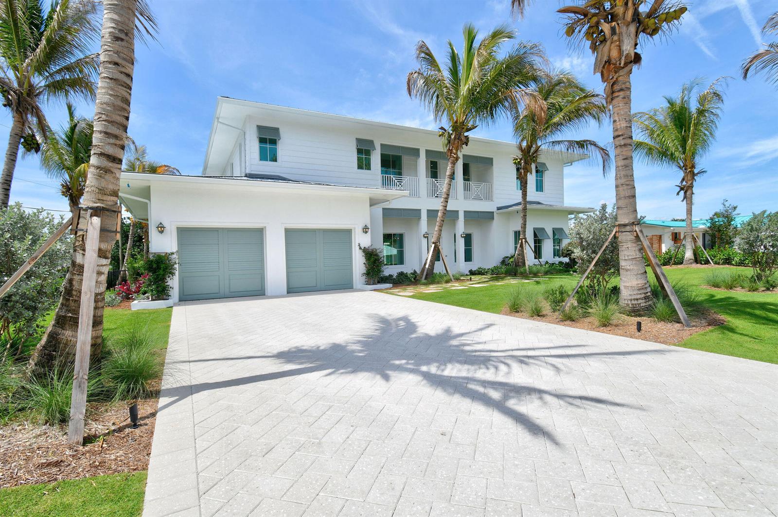 A two-story white house features a paved driveway, two garage doors, and several palm trees — 91 Golfview Drive, Tequesta FL 33469, TEQUESTA, FL