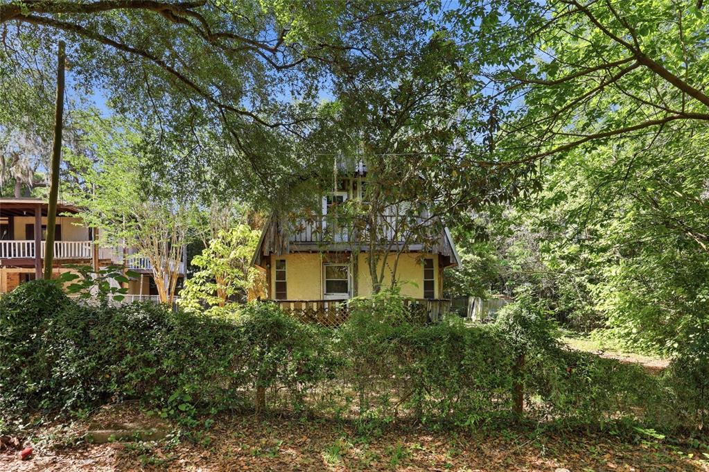A two-story yellow house with a balcony stands behind a dense, overgrown hedge — 20224 SE 156TH PLACE, UMATILLA, FL