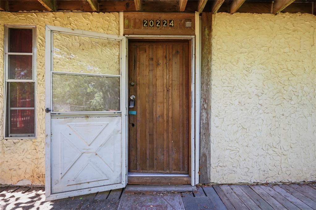 A wooden front door with a screen door sits on a porch with textured walls — 20224 SE 156TH PLACE, UMATILLA, FL