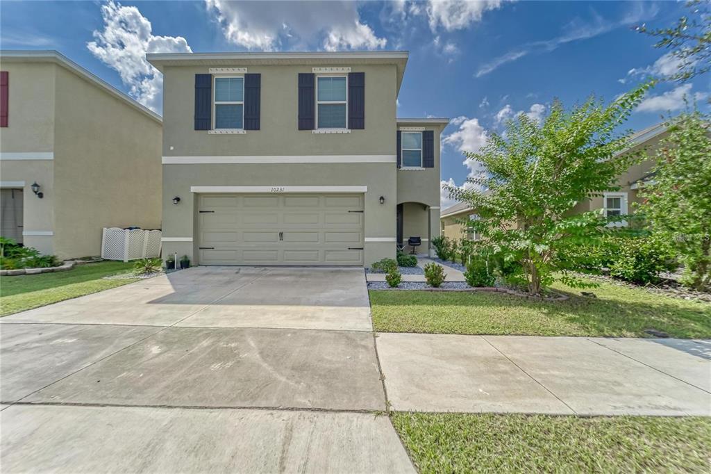 A two-story suburban house features a tan stucco exterior, a two-car garage, and shutters — 10231 GEESE TRAIL CIRCLE, SUN CITY CENTER, FL