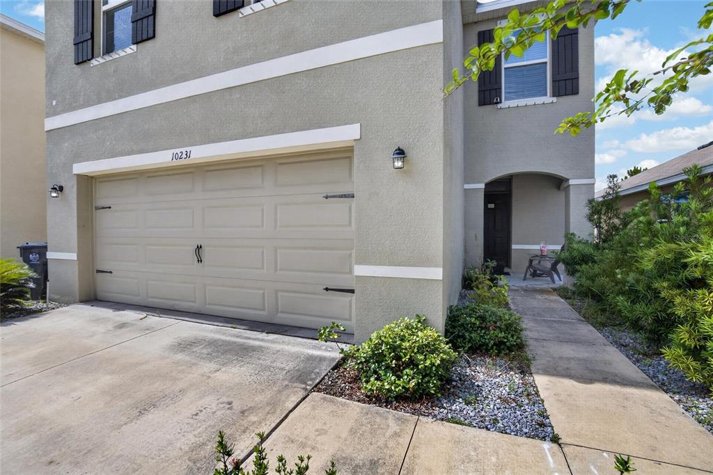 A two-story house exterior features a beige stucco facade, a garage, and a front entryway — 10231 GEESE TRAIL CIRCLE, SUN CITY CENTER, FL