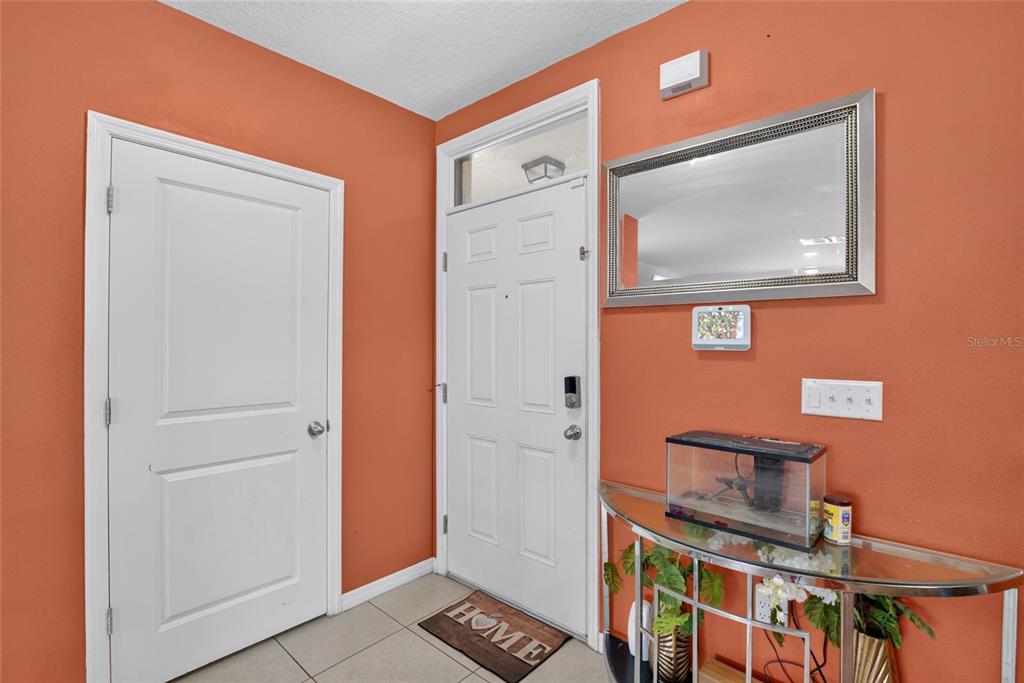 An entryway features orange walls, a white door, a glass console table, and a mirror — 10231 GEESE TRAIL CIRCLE, SUN CITY CENTER, FL