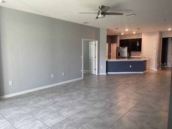 An open-concept living area features gray walls, tile flooring, a ceiling fan, and a kitchen — 1125 SAGUARO STREET, HAINES CITY, FL