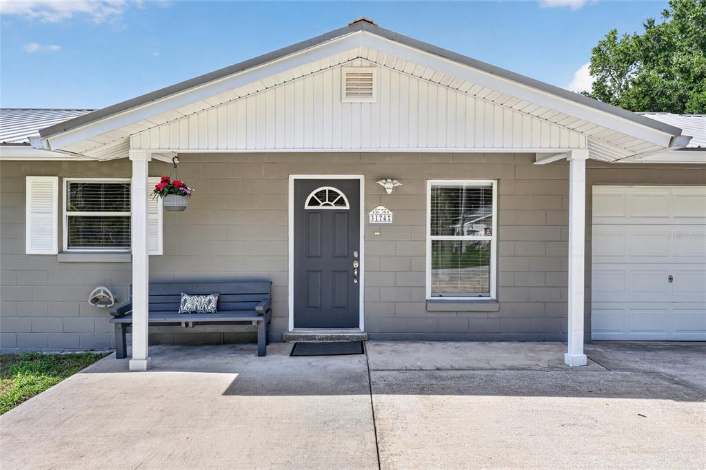 A gray concrete block house features a front porch, a dark door, and a garage — 3174 SE 6TH PLACE, OCALA, FL