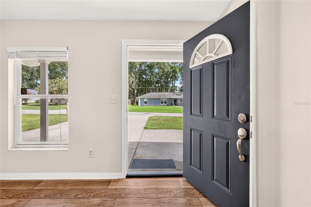An open dark gray front door reveals a view of a suburban street and house — 3174 SE 6TH PLACE, OCALA, FL