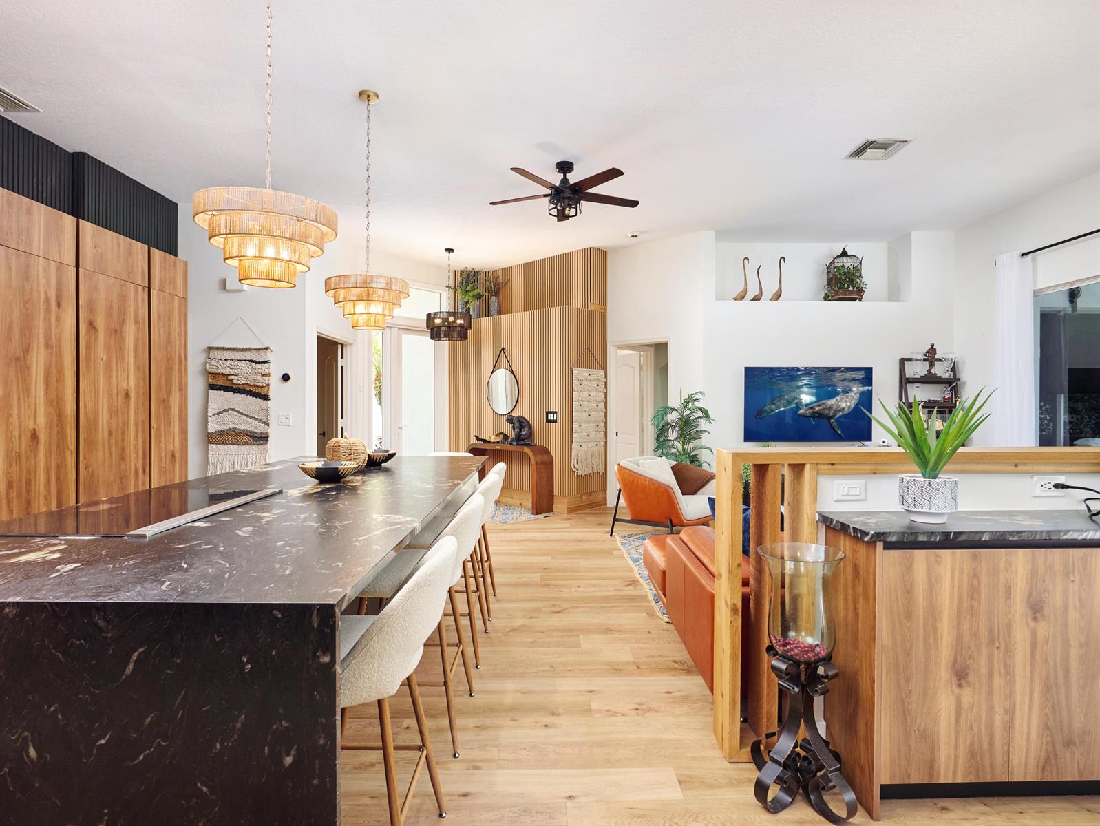 A modern kitchen and living area feature a large marble island, wood cabinetry, and slat-wall accents — 8166 Quail Meadow Way, West Palm Beach FL 33412, WEST PALM BEACH, FL