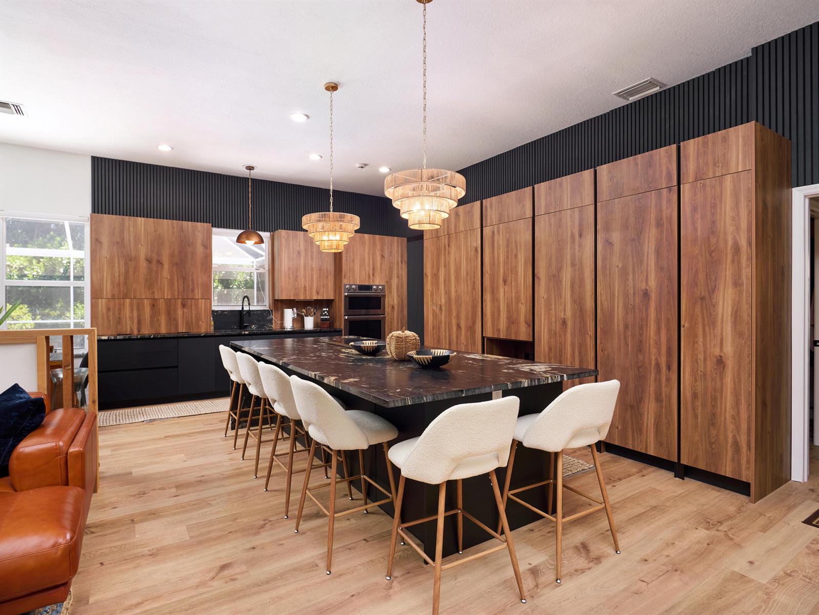 A modern kitchen features a large dark stone island, wood cabinetry, and white bar stools — 8166 Quail Meadow Way, West Palm Beach FL 33412, WEST PALM BEACH, FL