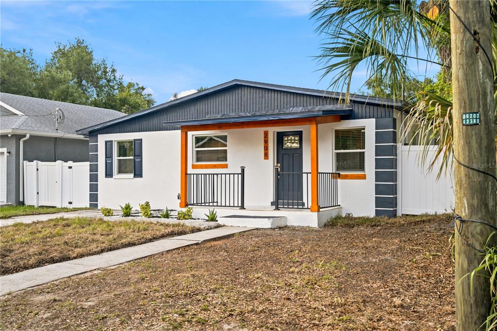 A single-story house with white stucco walls, dark blue trim, and a wooden front porch — 2908 E 26TH AVENUE, TAMPA, FL