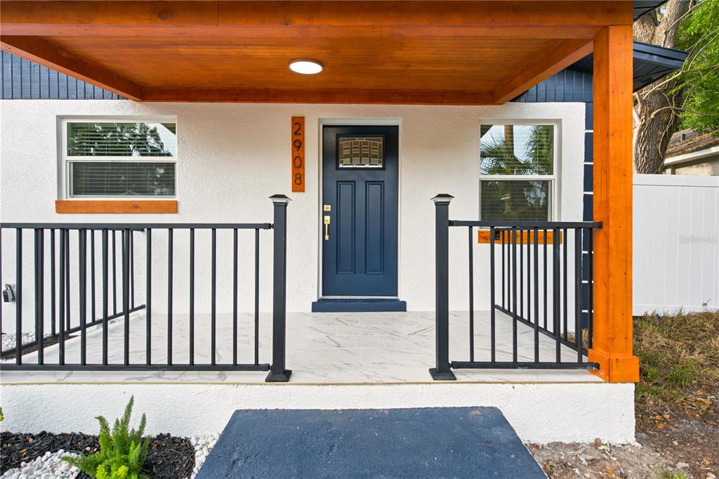 A front porch with a blue door, black railings, and a wood-paneled ceiling — 2908 E 26TH AVENUE, TAMPA, FL
