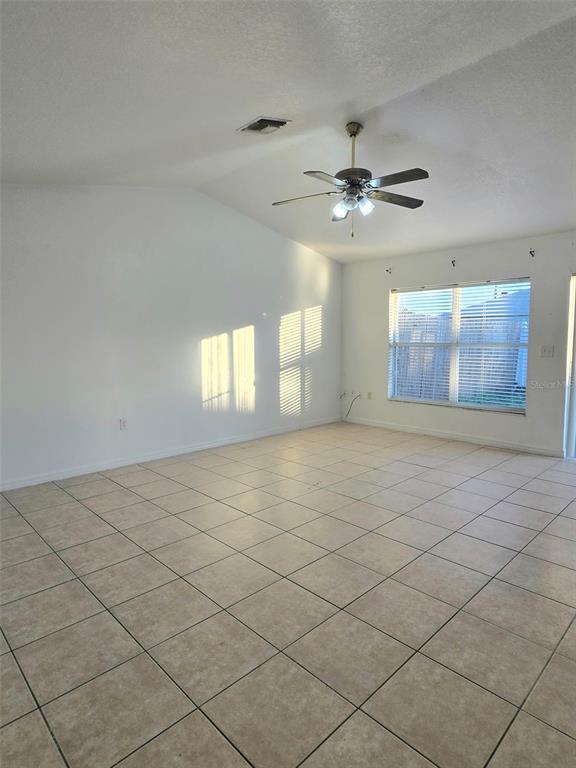 A spacious room features white walls, a vaulted ceiling with a fan, and tiled flooring — 737 BITTERN LANE, KISSIMMEE, FL