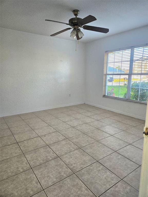 An empty room features light-colored tile flooring, white walls, and a ceiling fan — 737 BITTERN LANE, KISSIMMEE, FL