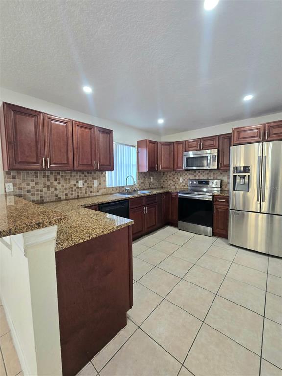 A kitchen features dark wood cabinets, granite countertops, stainless steel appliances, and tiled flooring — 737 BITTERN LANE, KISSIMMEE, FL