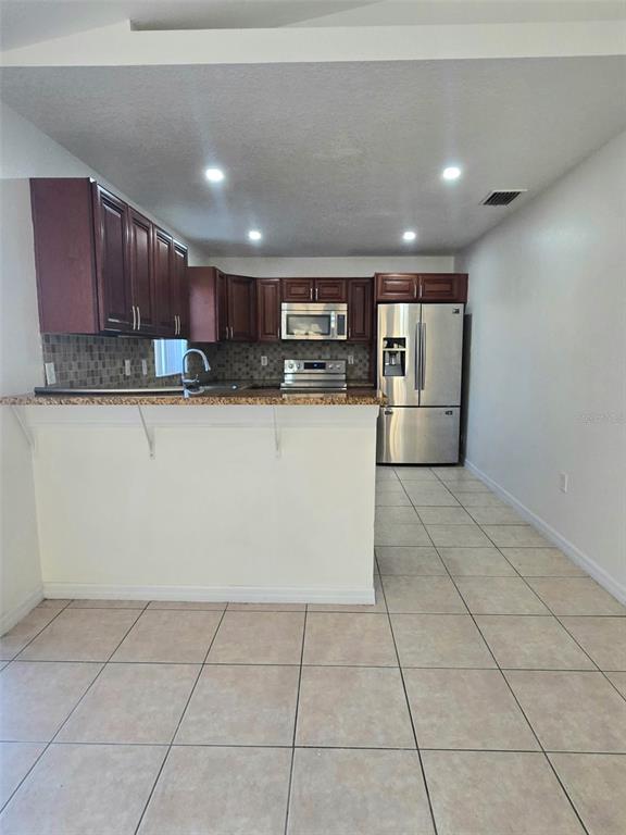 A kitchen features dark wood cabinets, stainless steel appliances, granite countertops, and tiled flooring — 737 BITTERN LANE, KISSIMMEE, FL