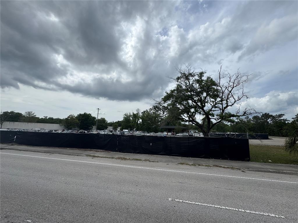 A black privacy fence encloses a parking lot filled with cars under a cloudy sky — 5515/5517 SHAD ROAD, JACKSONVILLE, FL