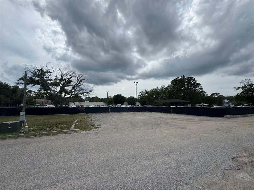 A gravel lot is enclosed by a black privacy fence under a cloudy sky — 5515/5517 SHAD ROAD, JACKSONVILLE, FL