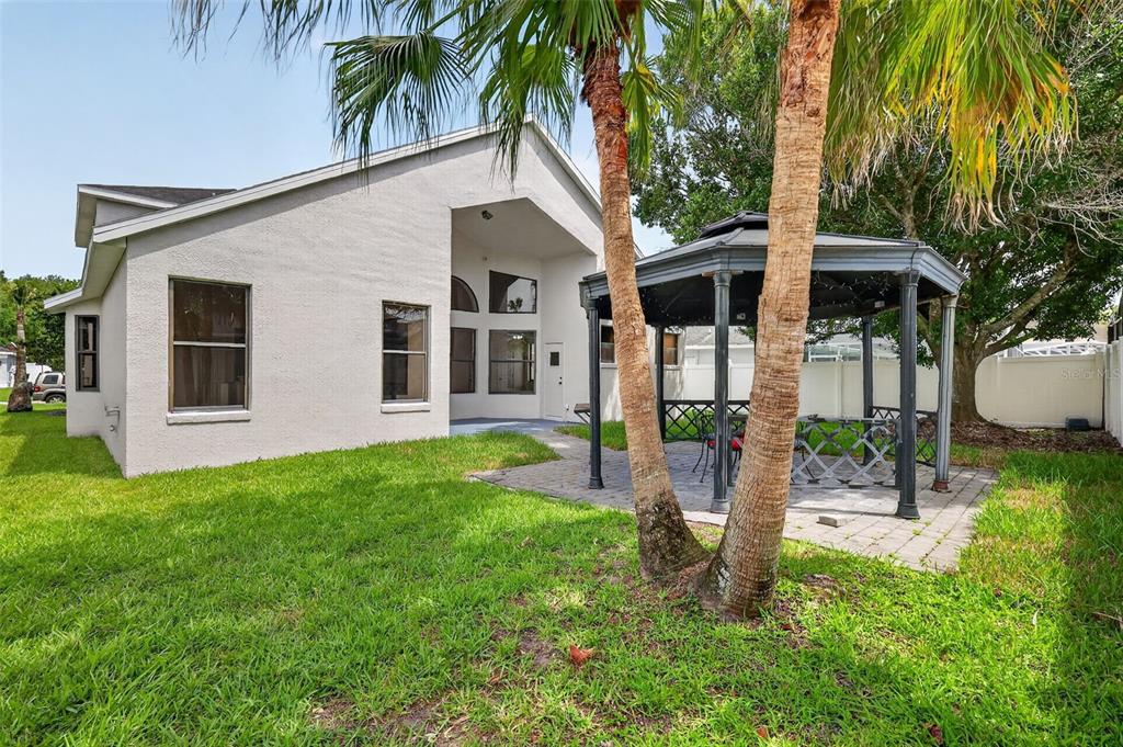 A backyard features a beige house, a paved patio, and a gazebo under palm trees — 12441 BOHANNON BOULEVARD, ORLANDO, FL