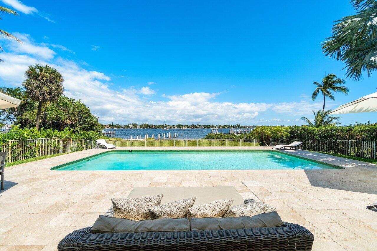 A swimming pool sits on a stone patio overlooking a bay with palm trees — 210 S Lake Drive, Lantana FL 33462, LANTANA, FL