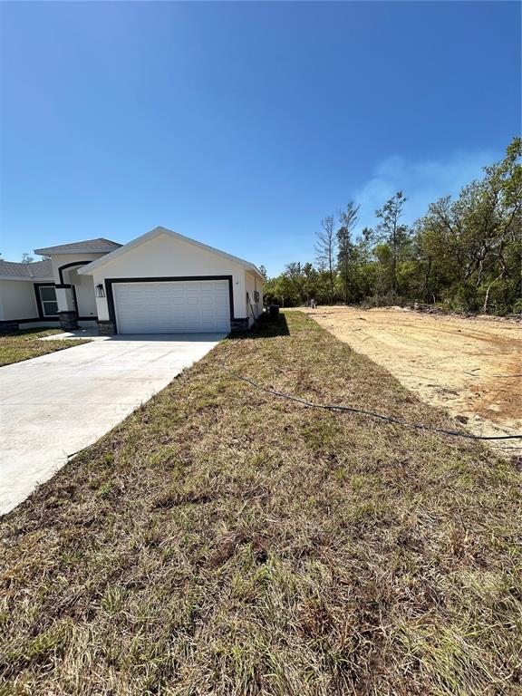 A single-story house with a white garage and a concrete driveway sits beside an empty lot — 13521 SW 106TH STREET, DUNNELLON, FL