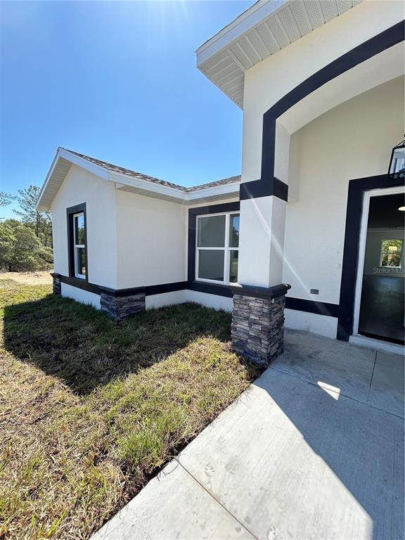 The exterior of a modern house features white stucco walls, dark trim, and stone accents — 13521 SW 106TH STREET, DUNNELLON, FL