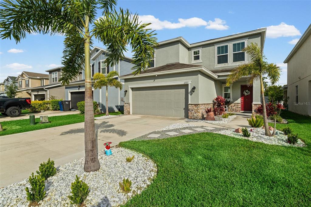 A two-story suburban house features a gray stucco exterior, stone accents, and a red door — 4327 REISSWOOD LOOP, PALMETTO, FL