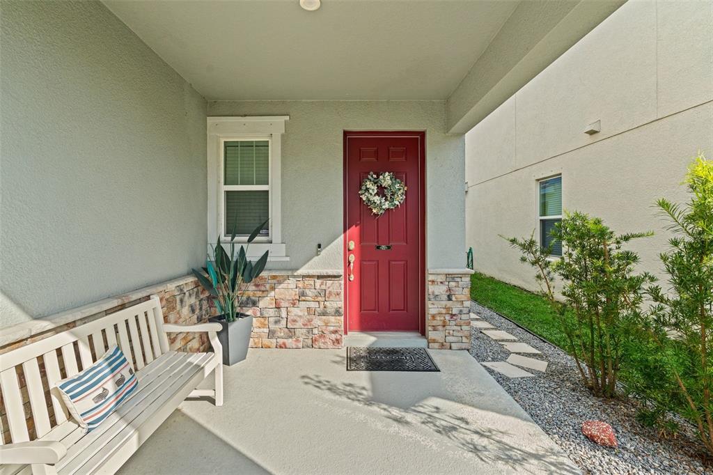 A covered front porch features a red door, stone veneer accents, and a white bench — 4327 REISSWOOD LOOP, PALMETTO, FL