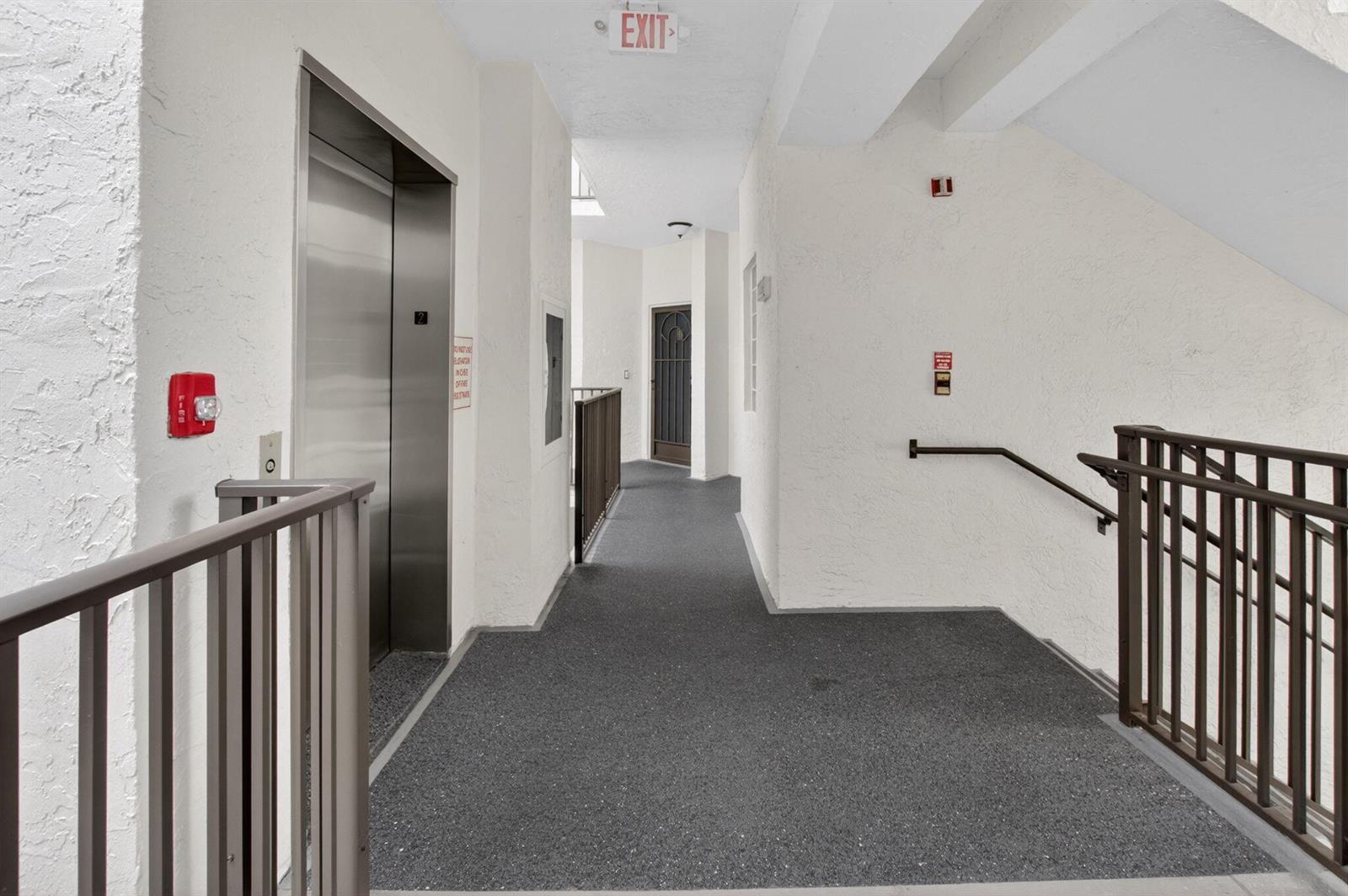A hallway features a metal elevator, a staircase with railings, and a dark door — 5153 Floria Drive # J, Boynton Beach FL 33437, BOYNTON BEACH, FL