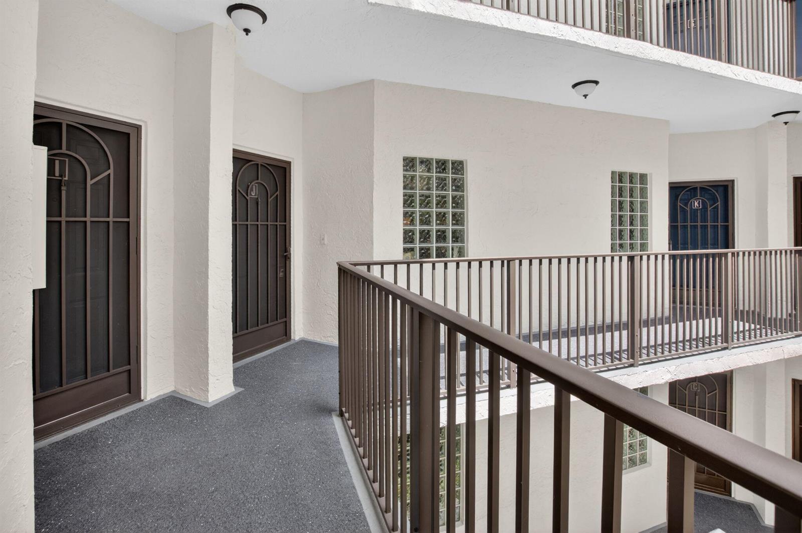 An outdoor apartment building walkway features brown metal railings, glass block windows, and numbered doors — 5153 Floria Drive # J, Boynton Beach FL 33437, BOYNTON BEACH, FL