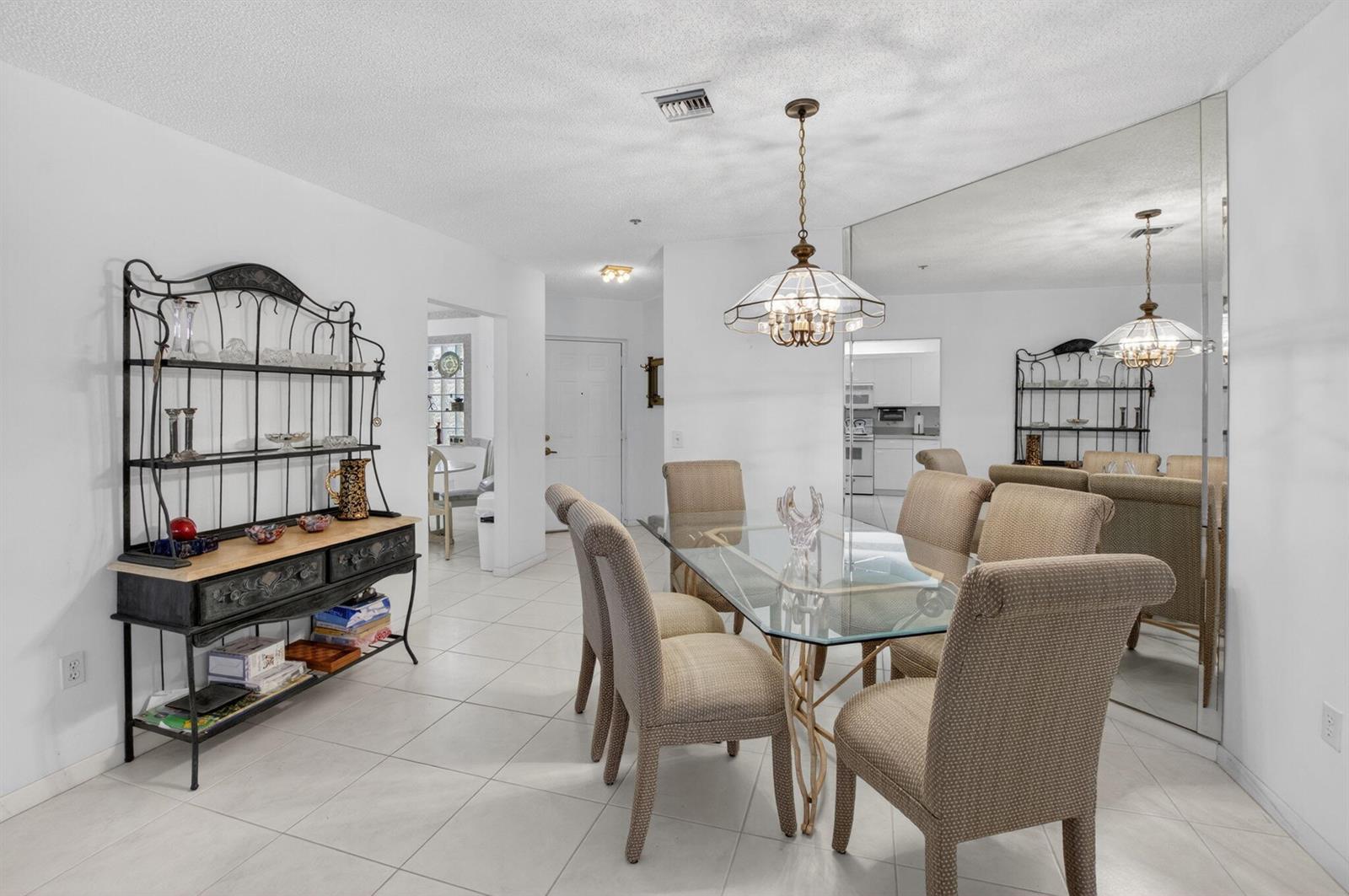 A dining room with a glass table, upholstered chairs, a metal hutch, and mirrored walls — 5153 Floria Drive # J, Boynton Beach FL 33437, BOYNTON BEACH, FL