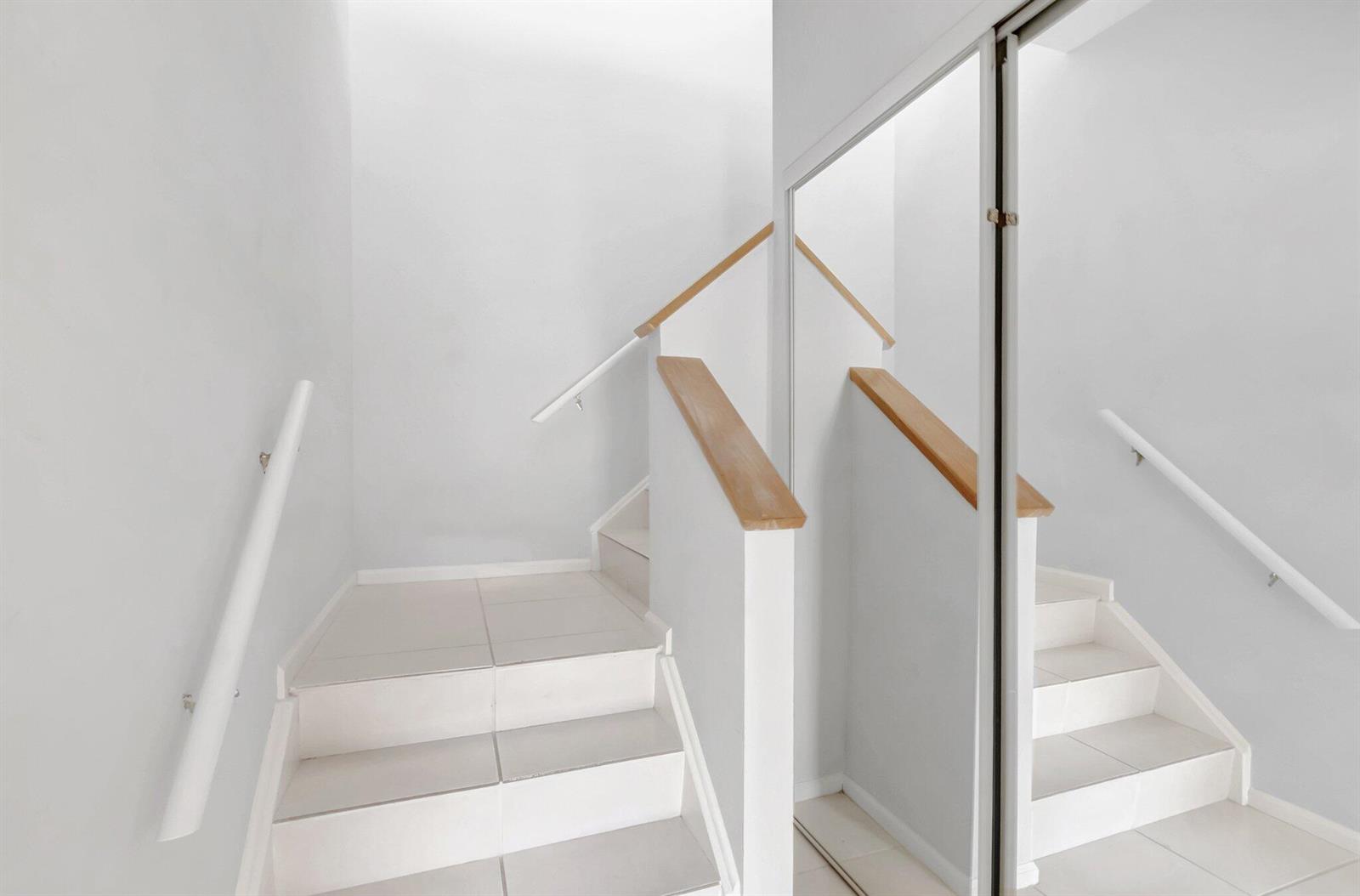 A staircase with white tiled steps, wooden handrails, and a large mirror on the wall — 6658 Montego Bay Boulevard # D, Boca Raton FL 33433, BOCA RATON, FL
