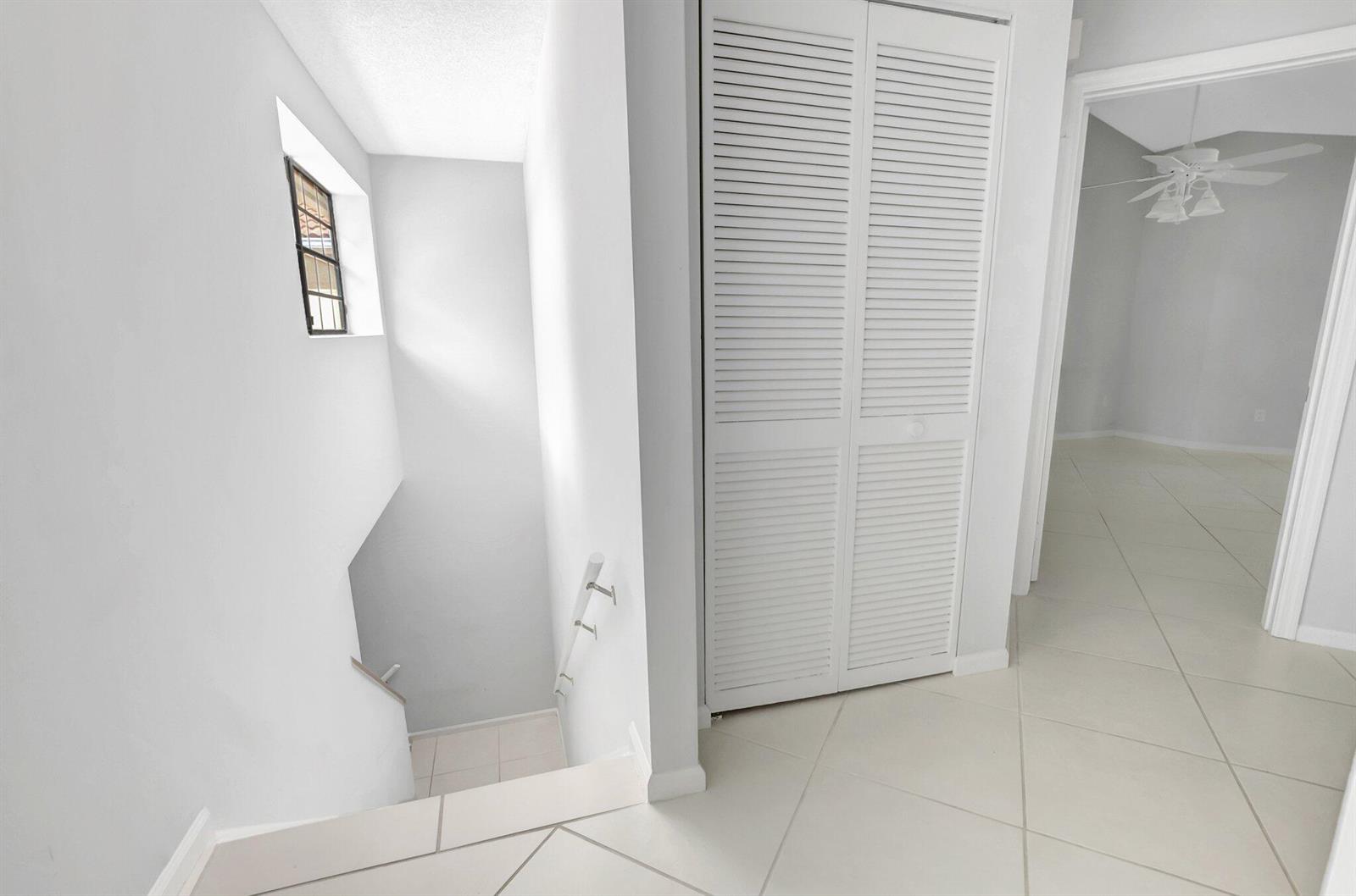 A white-tiled hallway features a louvered closet door and a staircase leading downward — 6658 Montego Bay Boulevard # D, Boca Raton FL 33433, BOCA RATON, FL