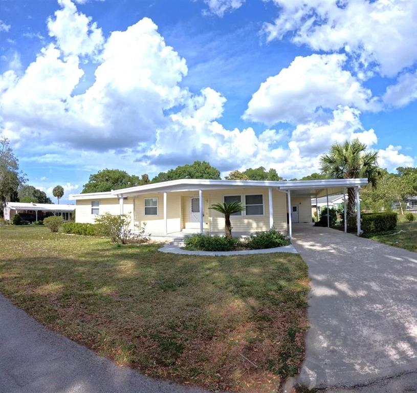A yellow single-story house with a covered carport and a front porch under a cloudy sky — 15 NE 63RD COURT, OCALA, FL