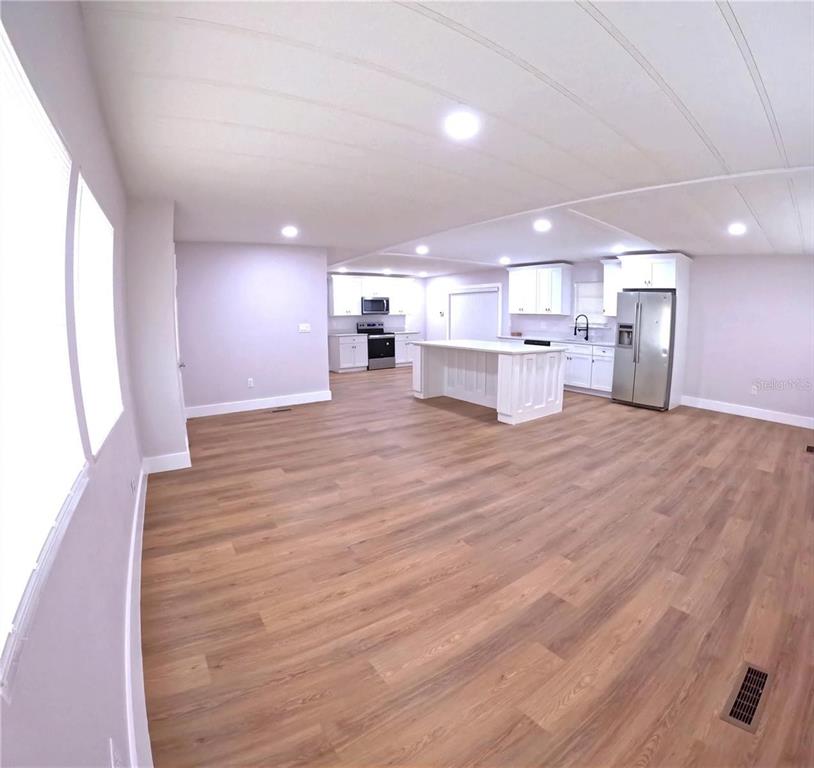 An open-concept kitchen features white cabinetry, a center island, and light wood-look flooring — 15 NE 63RD COURT, OCALA, FL