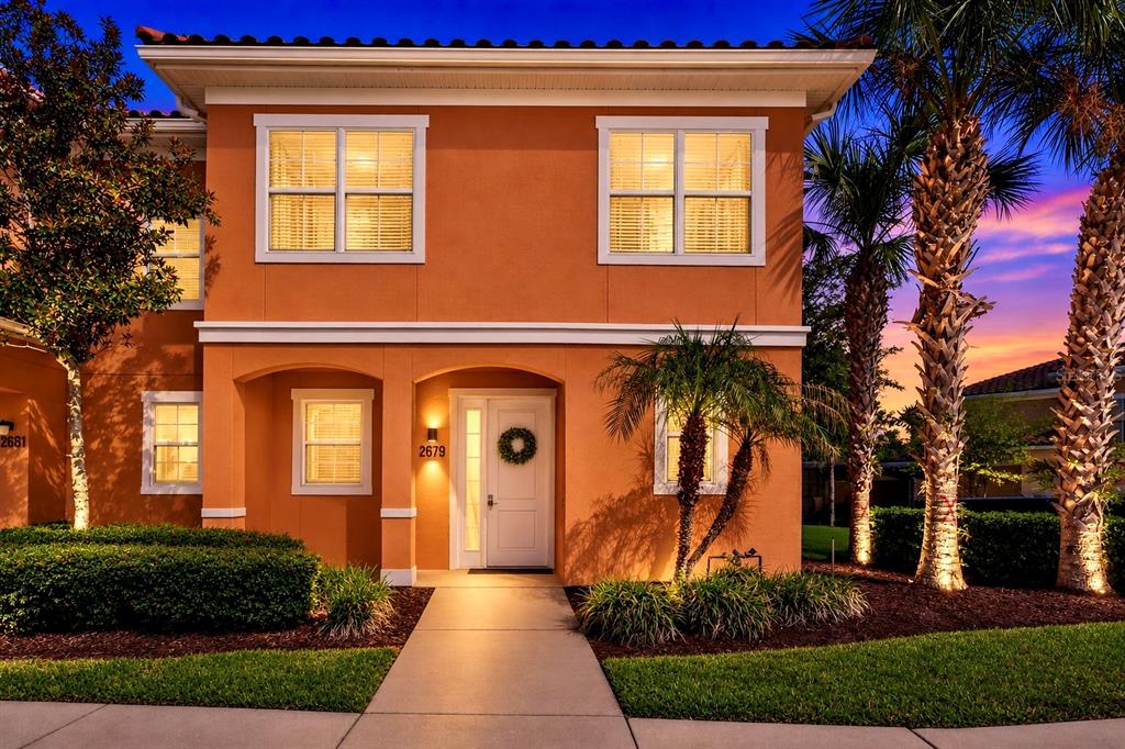 A two-story orange stucco house features a front entrance, palm trees, and a paved walkway — 2679 CORVETTE LANE, KISSIMMEE, FL
