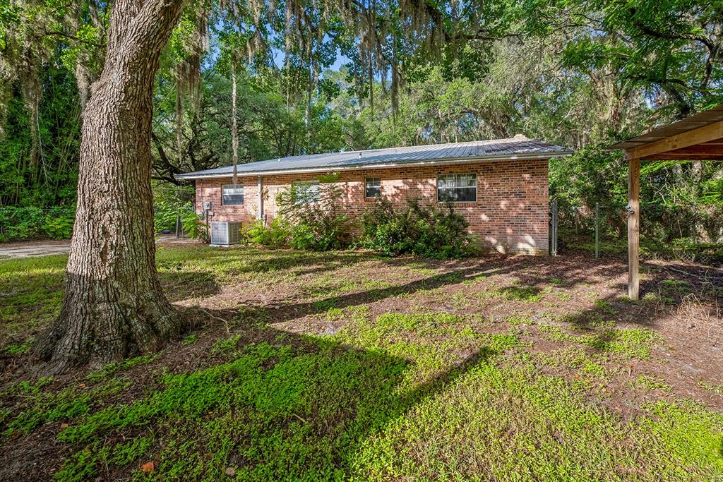 A single-story brick house sits in a wooded yard with a large tree in front — 7908 LAKE GENEVA LANE, KEYSTONE HEIGHTS, FL