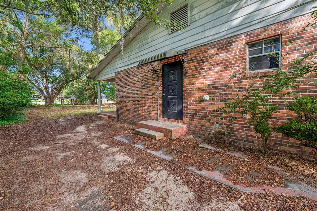 A brick house exterior features a black door, a small concrete step, and a porch — 7908 LAKE GENEVA LANE, KEYSTONE HEIGHTS, FL