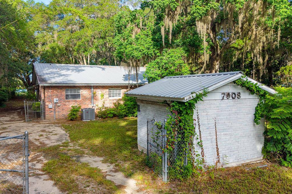 A single-story brick house with a metal roof sits in a wooded yard — 7908 LAKE GENEVA LANE, KEYSTONE HEIGHTS, FL