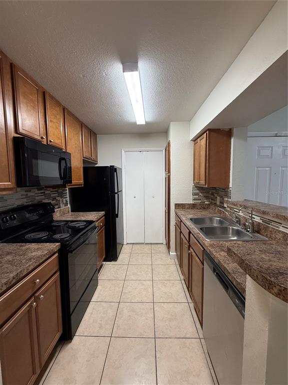 A galley kitchen features wood cabinets, black appliances, a double sink, and tiled flooring — 4367 THORNBRIAR LANE UNIT P208, ORLANDO, FL