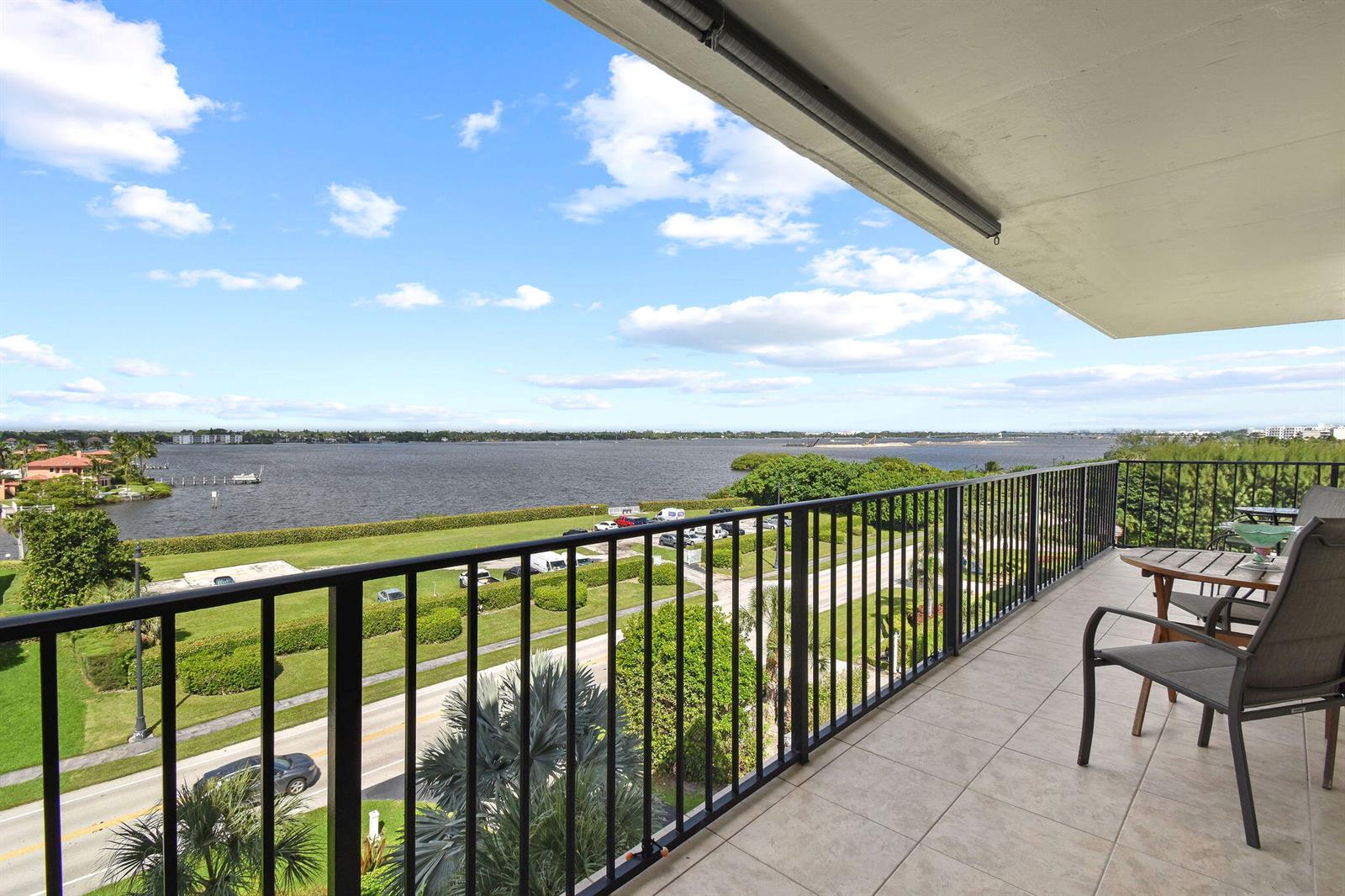 A balcony with tile flooring and metal railings overlooks a road, green space, and water — 3460 S Ocean Boulevard # 510, Palm Beach FL 33480, PALM BEACH, FL
