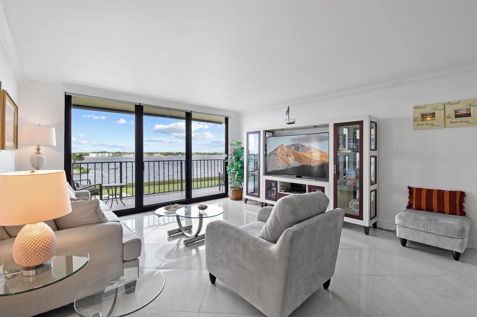 A living room features white tile floors, a large entertainment center, and a waterfront balcony view — 3460 S Ocean Boulevard # 510, Palm Beach FL 33480, PALM BEACH, FL
