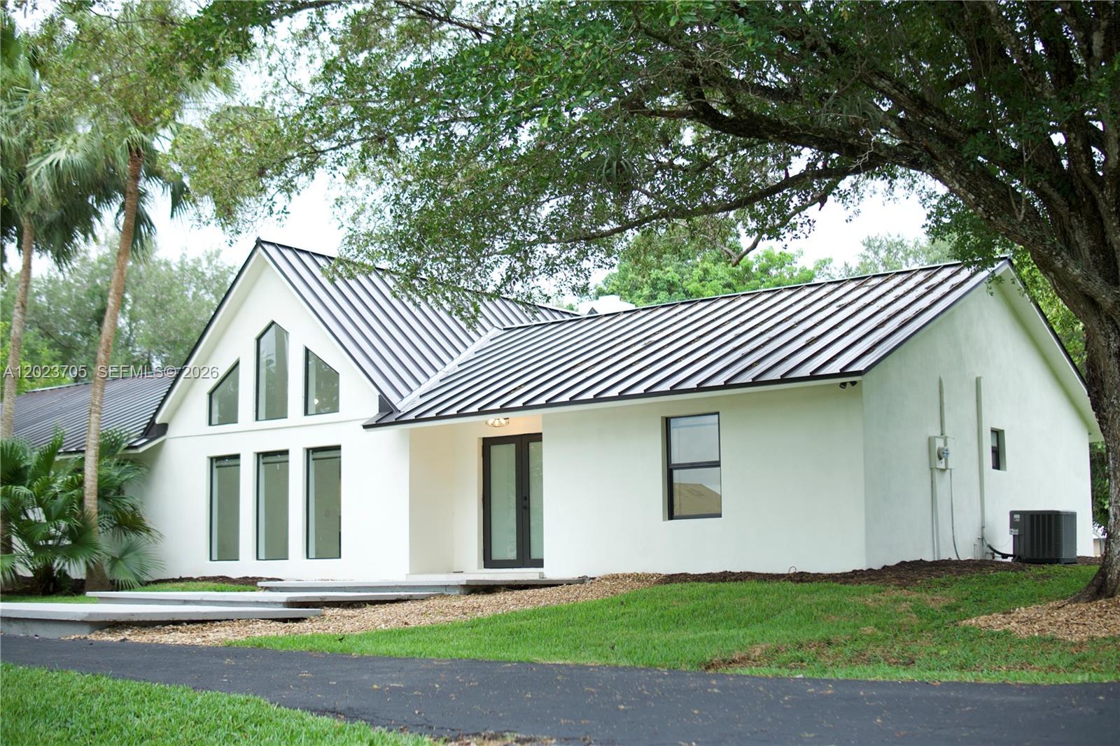 A white house with a black metal roof and large windows sits on a grassy lot — 20500 SW 50th Pl, Southwest Ranches FL 33332, SOUTHWEST RANCHES, FL