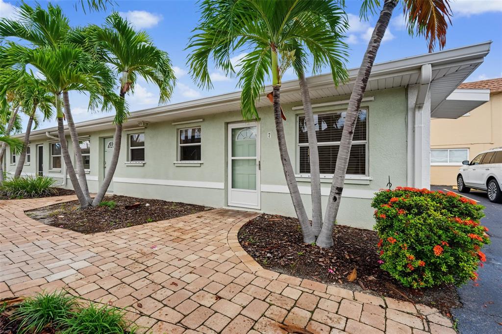 A single-story building with light green stucco walls, a brick walkway, and palm trees — 9040 BLIND PASS ROAD UNIT A7, ST PETERSBURG, FL