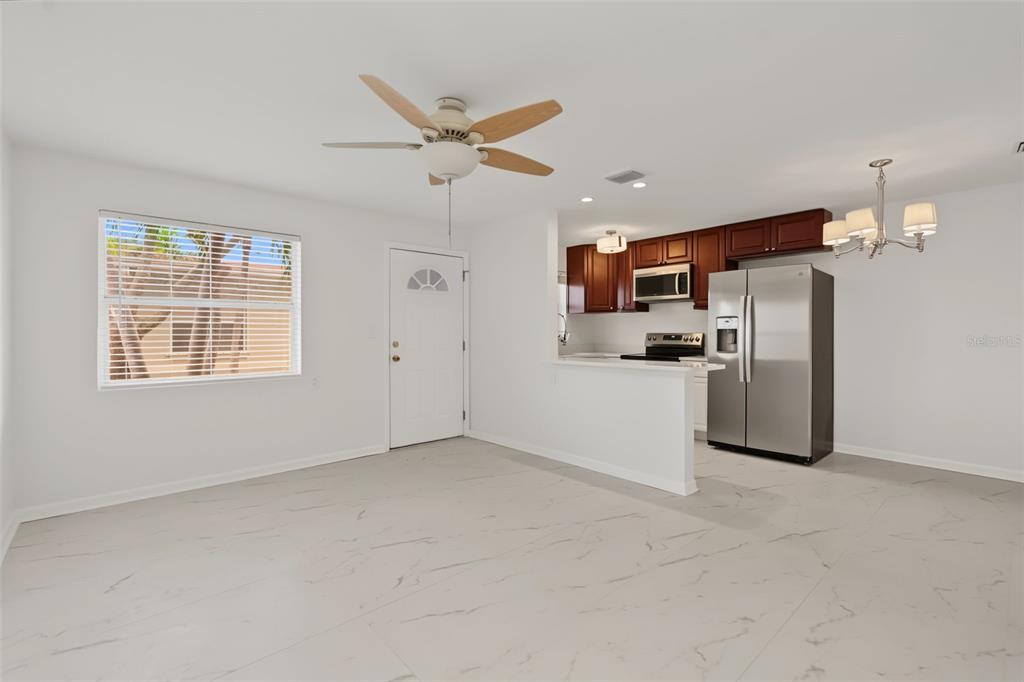 An open-concept kitchen and living area featuring white tile floors, dark wood cabinets, and appliances — 9040 BLIND PASS ROAD UNIT A7, ST PETERSBURG, FL