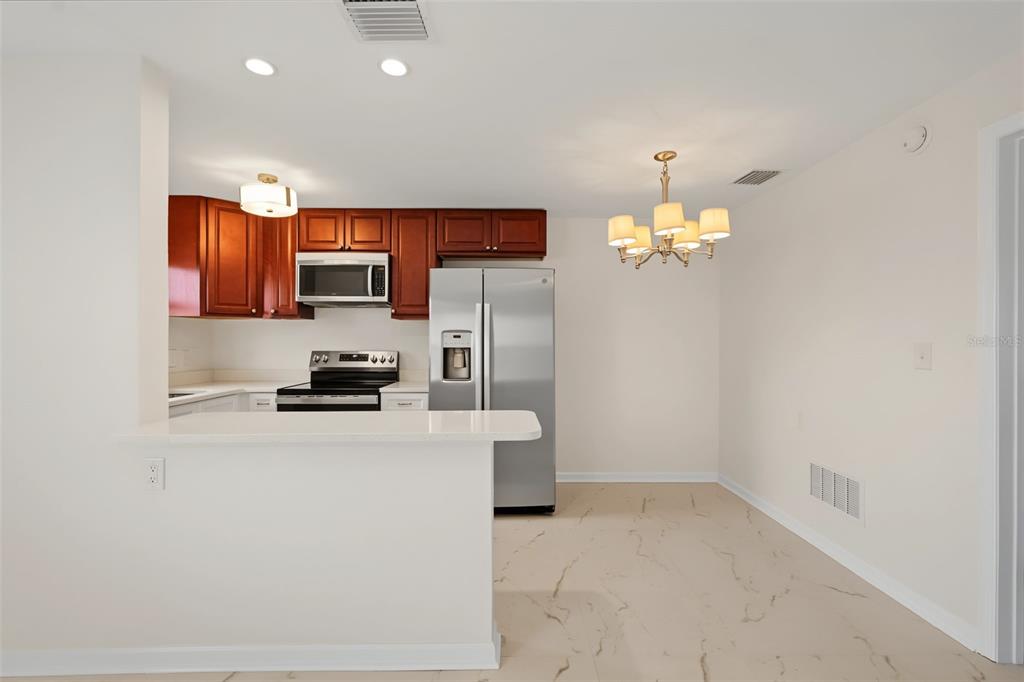 A kitchen with wood cabinets, stainless steel appliances, and a breakfast bar next to a dining area — 9040 BLIND PASS ROAD UNIT A7, ST PETERSBURG, FL
