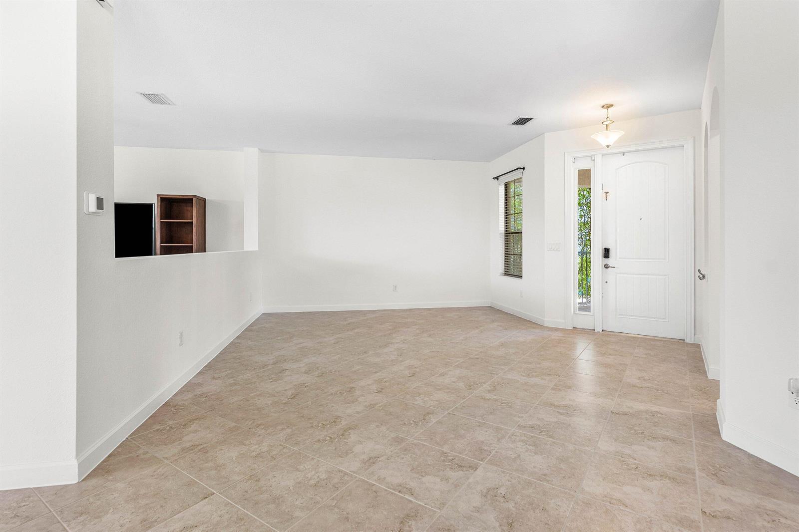 An empty living room features beige tile flooring, white walls, and a front entry door — 5428 Sandbirch Way, Lake Worth FL 33463, LAKE WORTH, FL