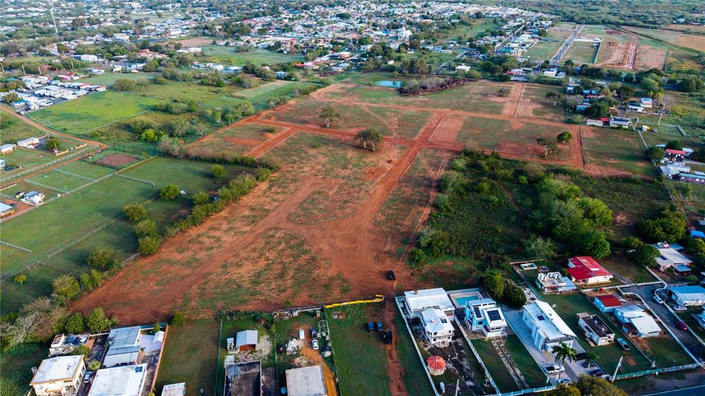 An aerial view shows a large, undeveloped dirt lot surrounded by residential houses and vegetation — Carretera 301 Km 0.6 COMBATE, CABO ROJO, PR