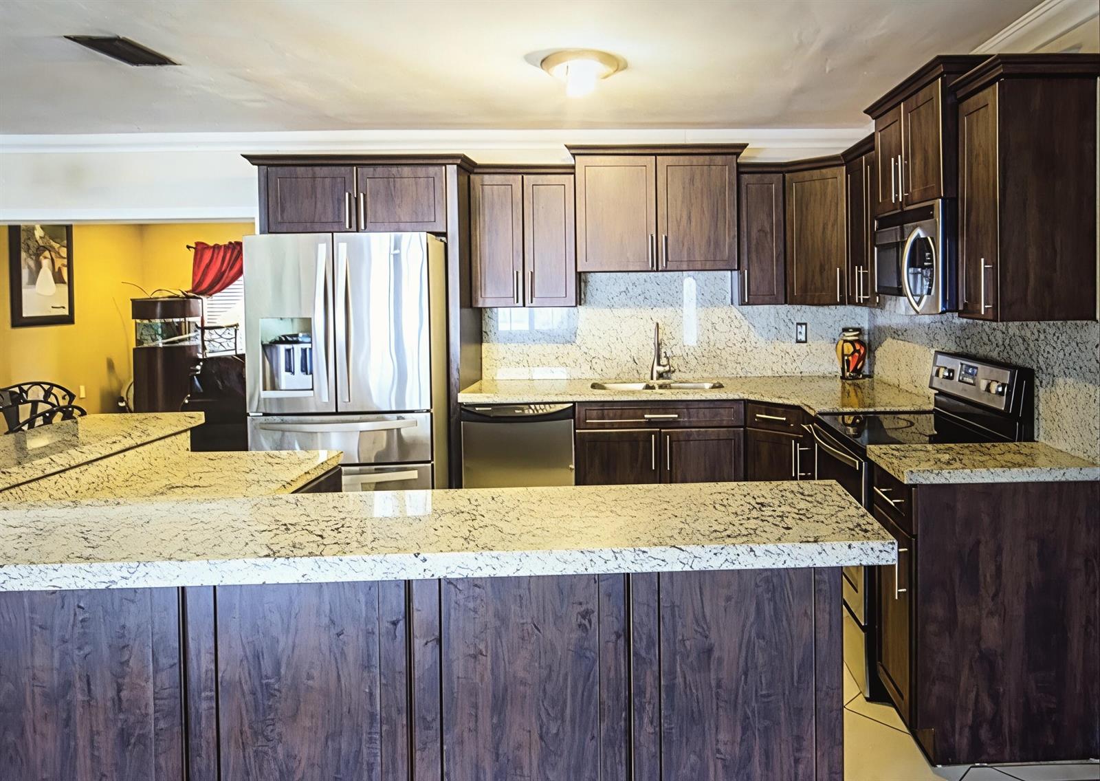 A kitchen features dark wood cabinets, granite countertops, and stainless steel appliances — 2441 PINE TREE Drive, Miramar FL 33023, MIRAMAR, FL