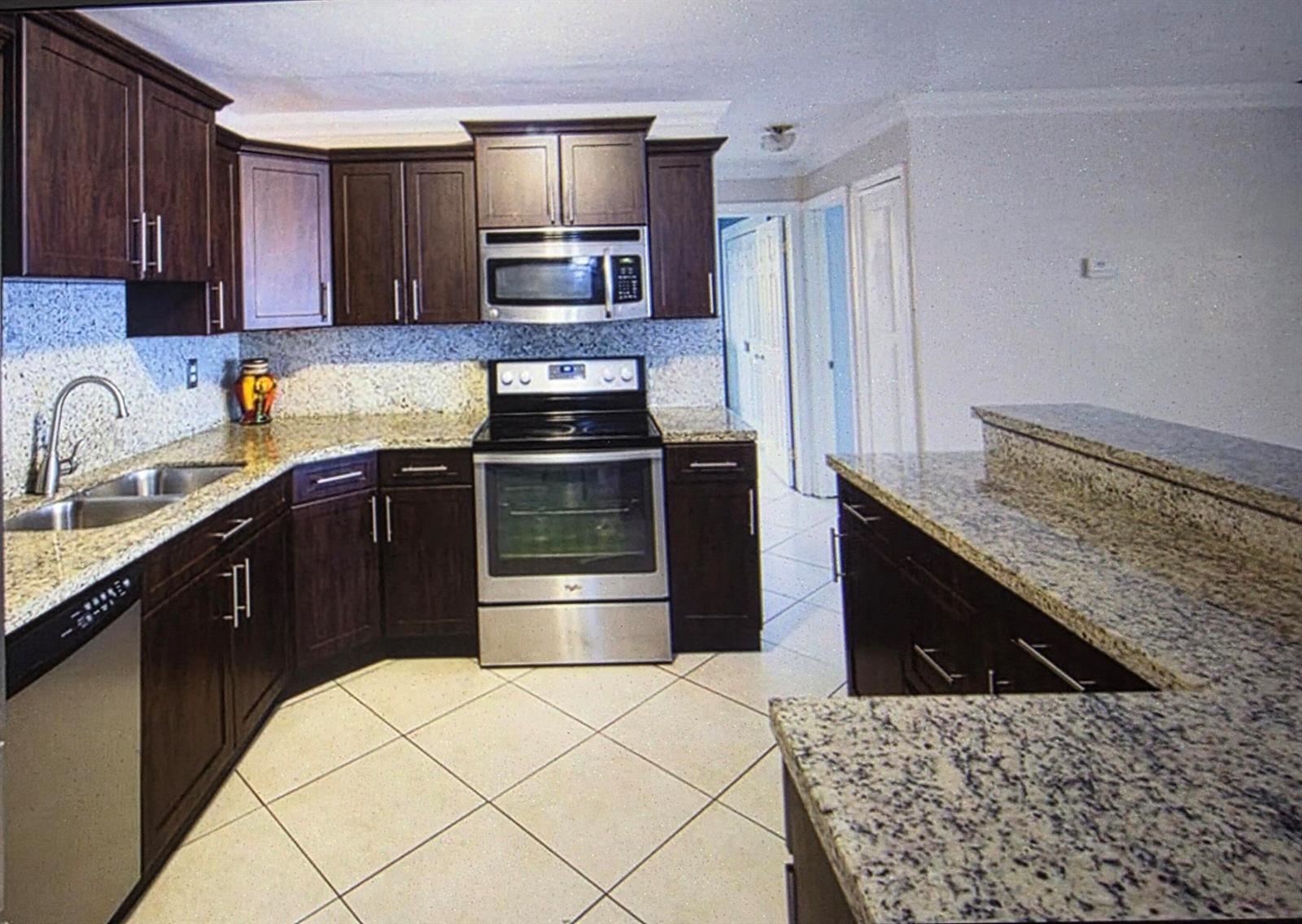 A kitchen features dark wood cabinets, granite countertops, stainless steel appliances, and diagonal floor tiles — 2441 PINE TREE Drive, Miramar FL 33023, MIRAMAR, FL