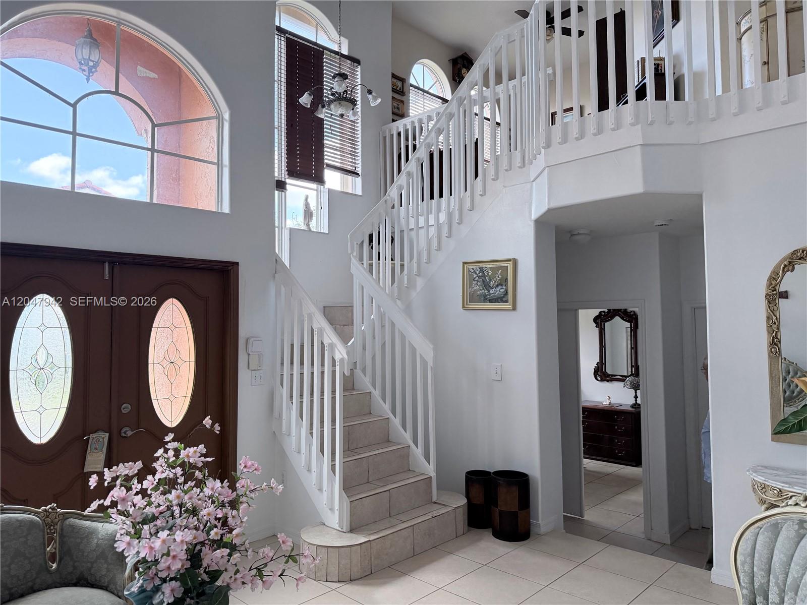 A bright foyer features a tiled staircase with white railings and high arched windows — 10824 NW 51st Ln, Doral FL 33178, DORAL, FL