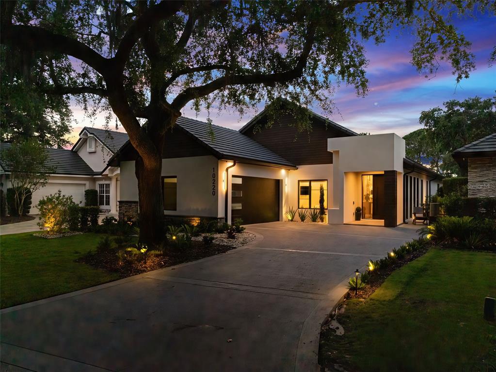 A modern house with a dark garage door and a concrete driveway at dusk — 10220 CHILTERN GARDEN DRIVE, ORLANDO, FL
